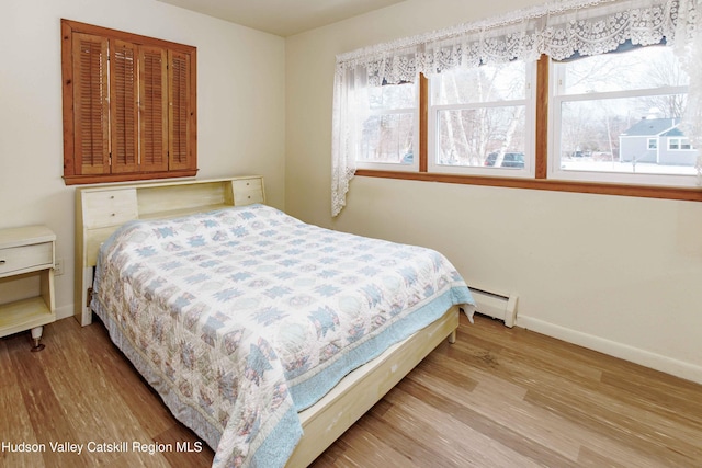 bedroom with multiple windows, a baseboard radiator, wood finished floors, and baseboards