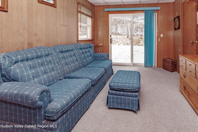 living area with a paneled ceiling, wood walls, and carpet