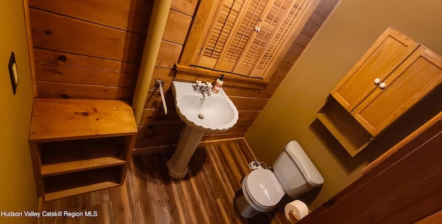 bathroom featuring sink, hardwood / wood-style floors, wooden walls, and toilet