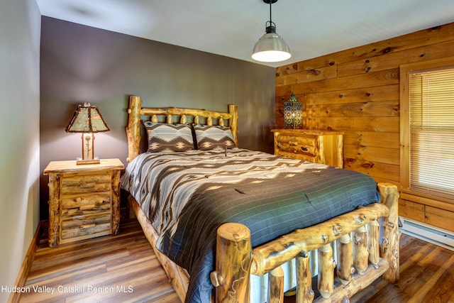 bedroom featuring hardwood / wood-style flooring, wood walls, and a baseboard heating unit