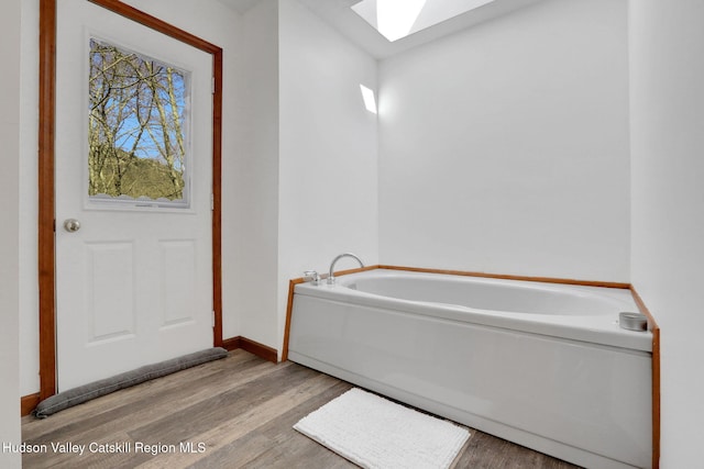 full bathroom featuring baseboards, wood finished floors, a garden tub, and a skylight