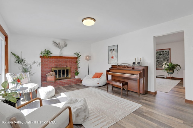 living area with baseboards, wood finished floors, a brick fireplace, and a baseboard radiator