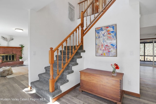 staircase featuring a brick fireplace, baseboards, and wood finished floors