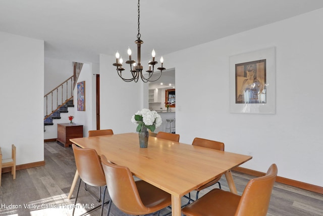 dining room with light wood finished floors, baseboards, a notable chandelier, and stairway