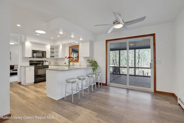 kitchen with a breakfast bar area, black appliances, light wood-type flooring, and white cabinetry