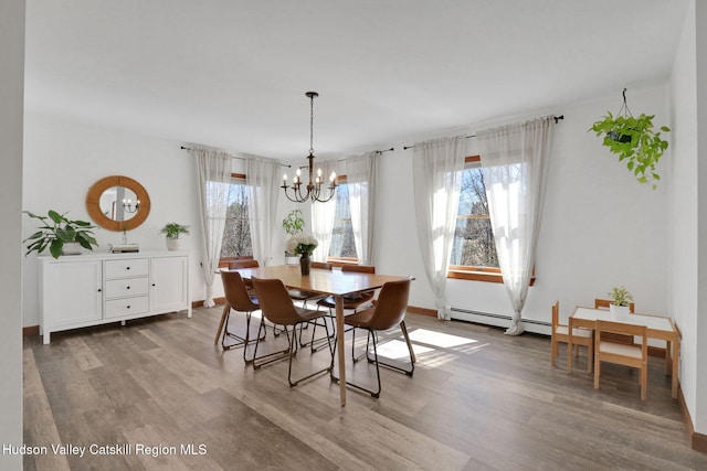 dining room featuring a notable chandelier, baseboards, a baseboard heating unit, and wood finished floors