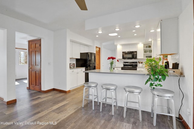 kitchen featuring white cabinets, wood finished floors, a peninsula, baseboards, and black appliances