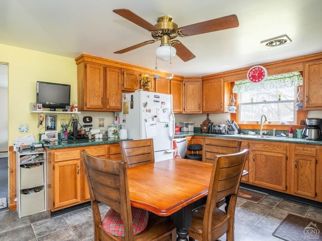 kitchen with freestanding refrigerator, a sink, ceiling fan, and brown cabinets