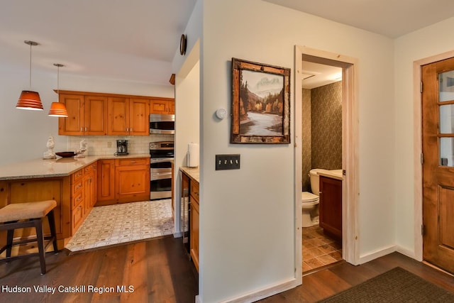122 Brainard Ridge Rd Unit 14F, Windham, NY 12496 - kitchen with dark wood-type flooring, appliances with stainless steel finishes, a peninsula, backsplash, and hanging light fixtures