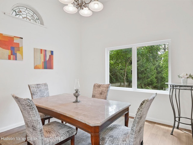 dining area with a towering ceiling, light wood-type flooring, and an inviting chandelier