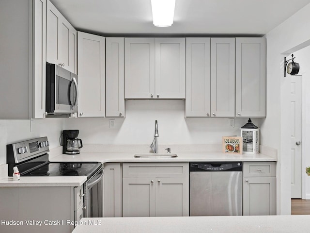 kitchen with hardwood / wood-style floors, appliances with stainless steel finishes, gray cabinetry, and sink