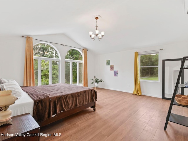 bedroom with light wood-type flooring, an inviting chandelier, and lofted ceiling