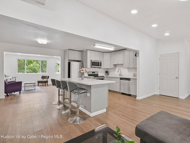 kitchen with sink, stainless steel appliances, light hardwood / wood-style floors, a breakfast bar, and a kitchen island