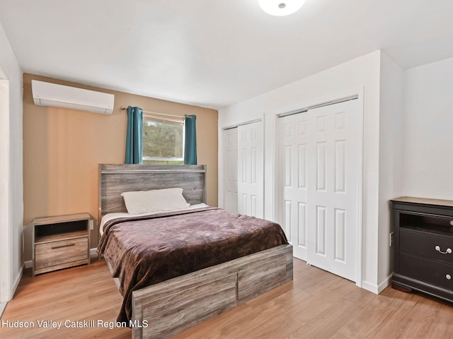 bedroom with an AC wall unit, multiple closets, and light wood-type flooring