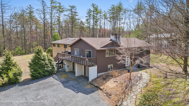 view of side of home featuring an attached garage, a chimney, aphalt driveway, and a deck