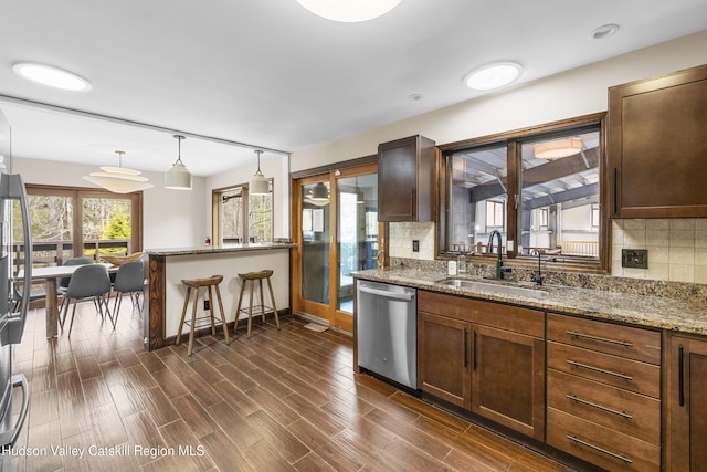 kitchen with stainless steel dishwasher, a sink, dark wood-type flooring, baseboards, and a peninsula