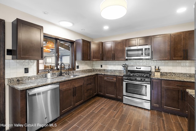 kitchen featuring stone counters, dark brown cabinetry, stainless steel appliances, and a sink