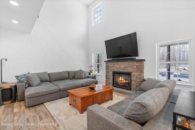 living room featuring a towering ceiling, a stone fireplace, and light hardwood / wood-style floors