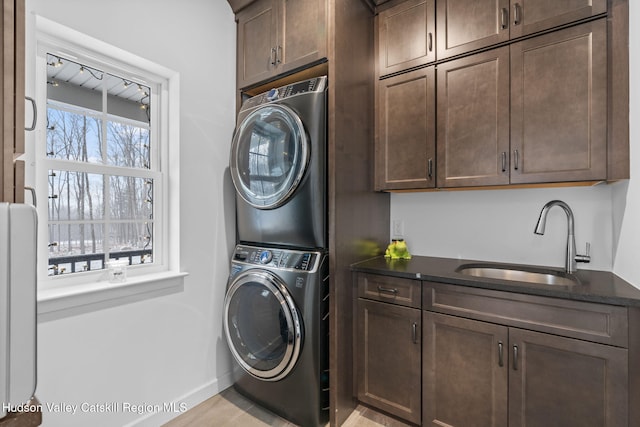 washroom with cabinets, a healthy amount of sunlight, stacked washer and clothes dryer, and sink