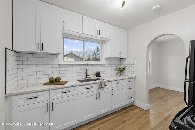 kitchen featuring white cabinetry, sink, black fridge, light hardwood / wood-style floors, and decorative backsplash