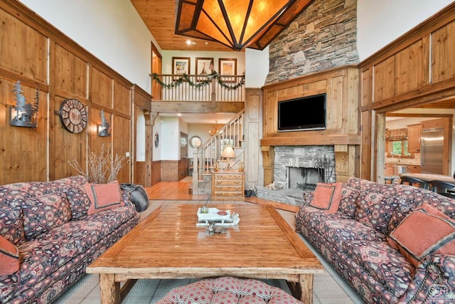 19 Twin Maples Ln, Windham, NY 12496 - living room featuring high vaulted ceiling, stairs, wood walls, a stone fireplace, and wainscoting