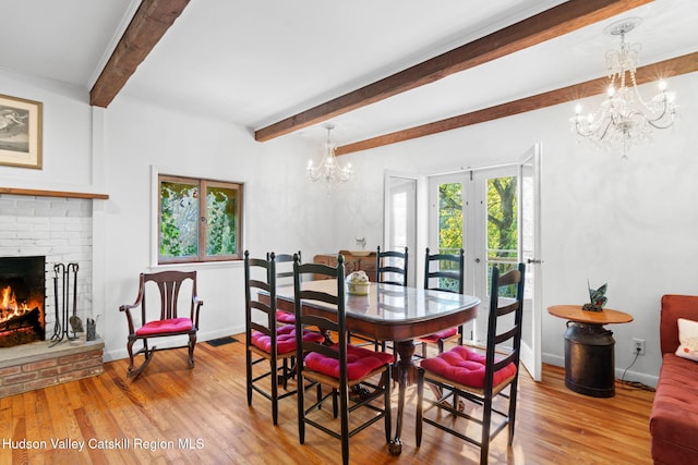 dining space with beam ceiling, a fireplace, light hardwood / wood-style floors, and french doors