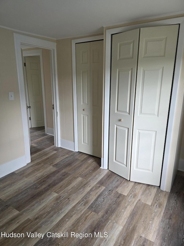 unfurnished bedroom with wood finished floors, baseboards, and multiple closets