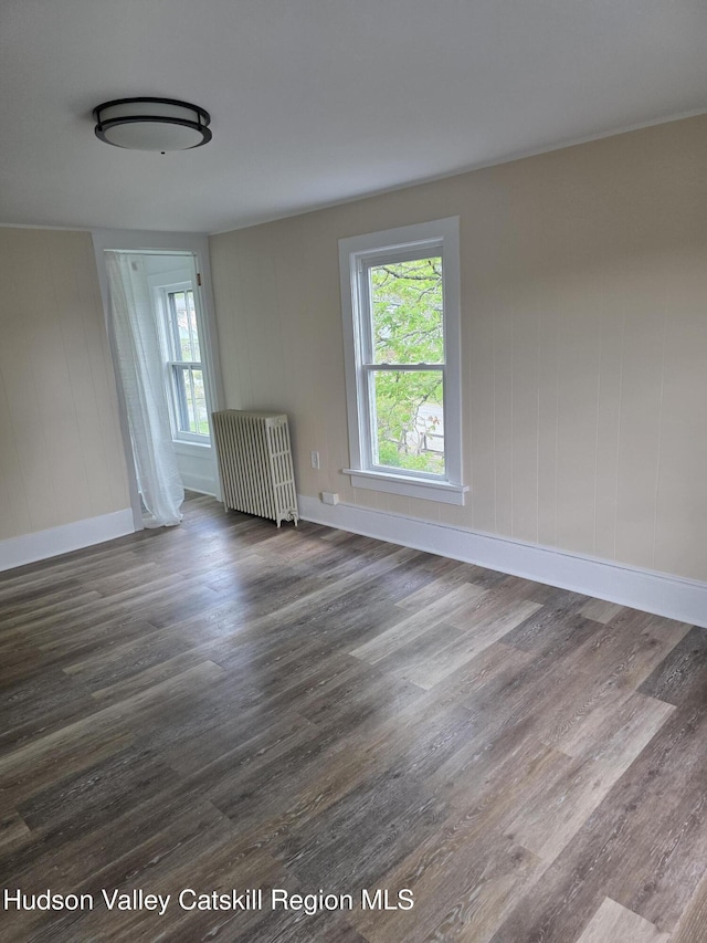 spare room with radiator, healthy amount of natural light, dark wood-style floors, and baseboards