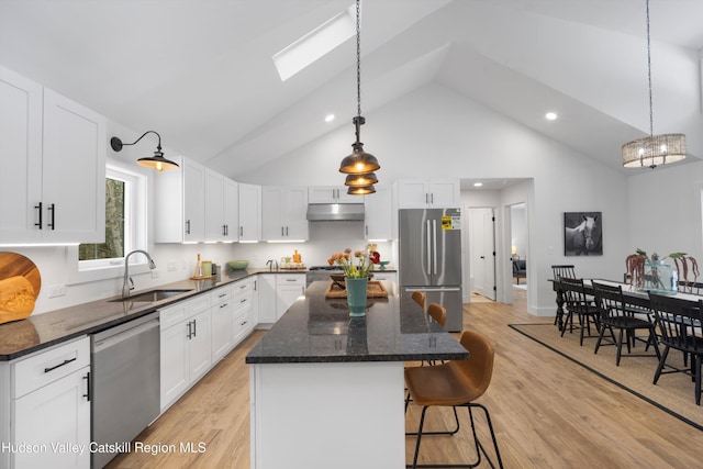 kitchen with appliances with stainless steel finishes, white cabinetry, a sink, a kitchen island, and under cabinet range hood