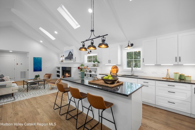 kitchen with a warm lit fireplace, a skylight, open floor plan, and a sink