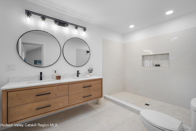 bathroom with toilet, double vanity, a sink, and tiled shower