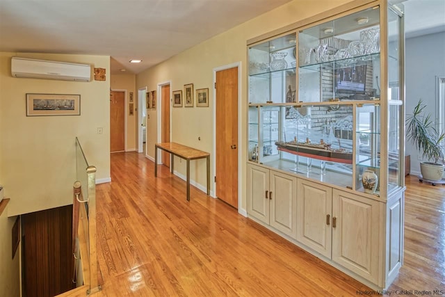 bar with light wood-type flooring, a wall mounted AC, and light brown cabinets