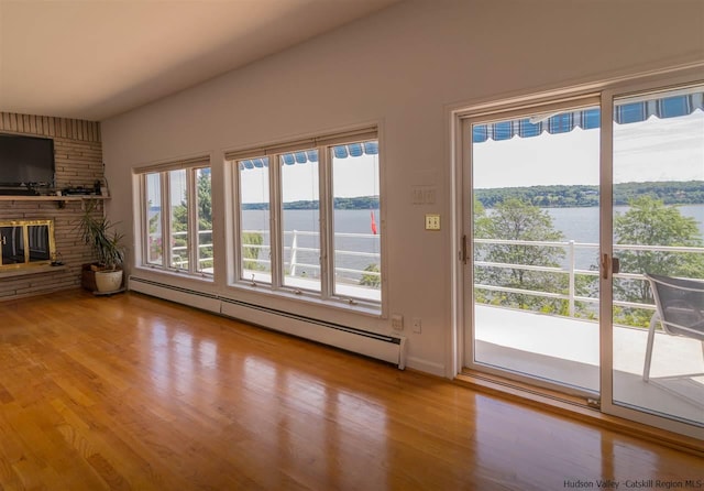 unfurnished living room featuring a baseboard radiator, a large fireplace, hardwood / wood-style floors, and a water view