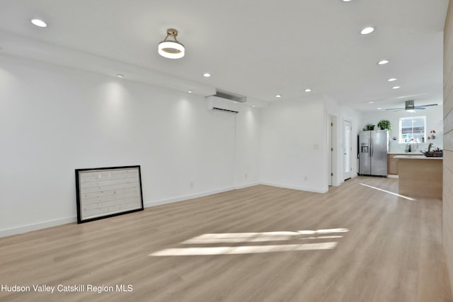 spare room with light hardwood / wood-style floors, a wall unit AC, and ceiling fan