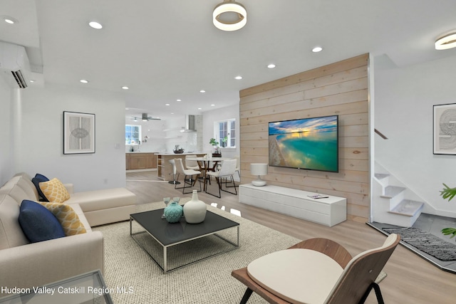 living room with a wall unit AC, wood walls, light hardwood / wood-style flooring, and ceiling fan