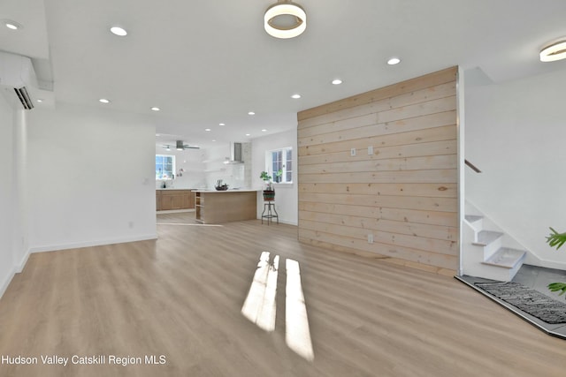 unfurnished living room featuring a wall mounted air conditioner, sink, light wood-type flooring, and wooden walls