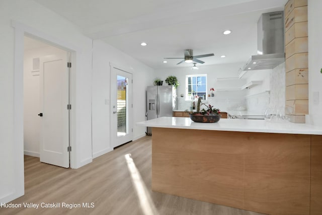 kitchen with wall chimney exhaust hood, stainless steel refrigerator with ice dispenser, tasteful backsplash, kitchen peninsula, and light wood-type flooring