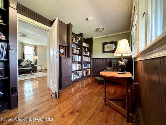 living area featuring hardwood / wood-style floors, a baseboard heating unit, a wainscoted wall, and ornamental molding