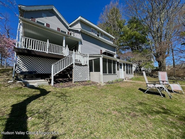 back of property featuring a wooden deck, a sunroom, stairs, and a lawn