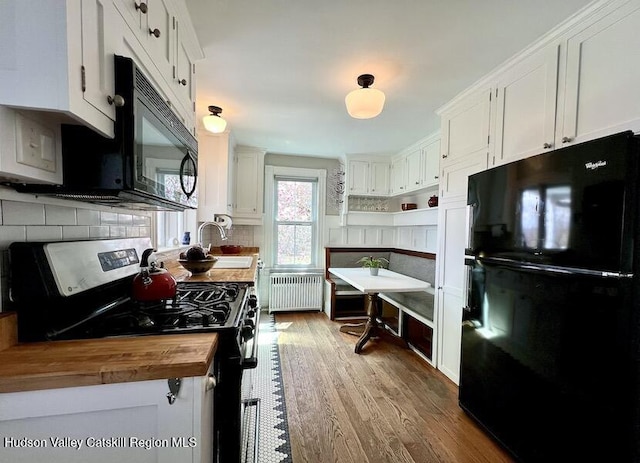 kitchen with radiator heating unit, wood finished floors, black appliances, wood counters, and backsplash