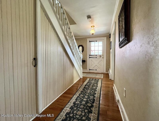 entryway with a baseboard radiator, baseboards, crown molding, and wood finished floors