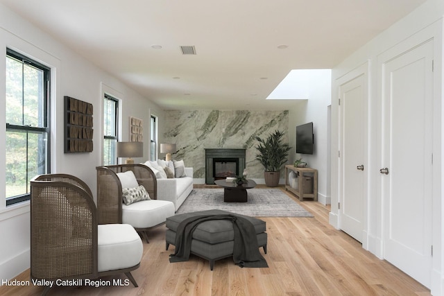 living room featuring visible vents, a healthy amount of sunlight, light wood-style floors, and a high end fireplace