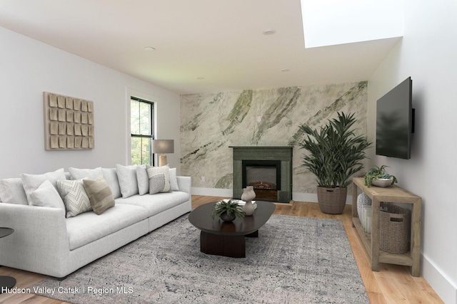 living room with wood finished floors, baseboards, a premium fireplace, a skylight, and an accent wall