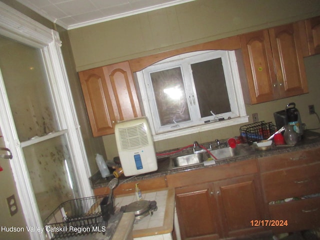 kitchen with ornamental molding, tile counters, a sink, and brown cabinets