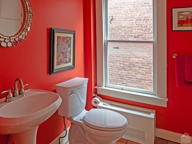 half bathroom with radiator heating unit, a sink, and toilet