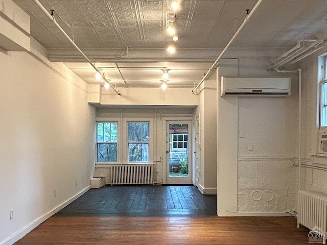 basement with radiator, wood-type flooring, a wall mounted AC, and baseboards