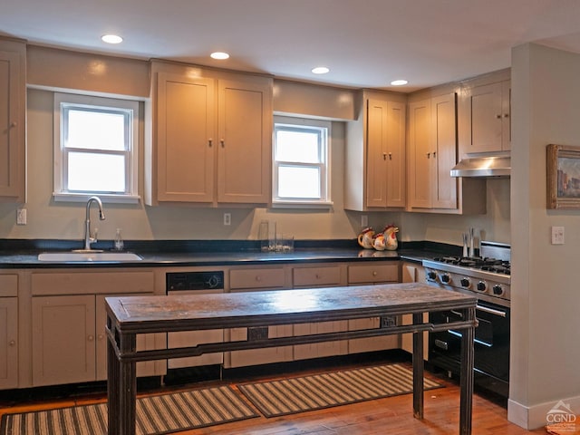 kitchen with gas range, under cabinet range hood, a sink, dark countertops, and light wood-style floors