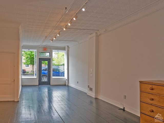 spare room featuring rail lighting, dark wood finished floors, and baseboards