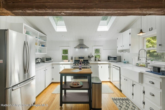 kitchen with wall chimney exhaust hood, white cabinetry, appliances with stainless steel finishes, and light hardwood / wood-style flooring