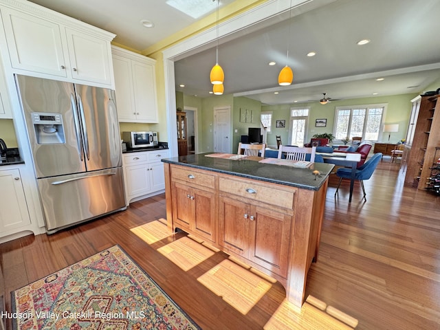 kitchen with stainless steel appliances, a kitchen island, wood finished floors, white cabinets, and open floor plan